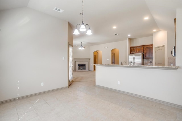 kitchen featuring light stone countertops, appliances with stainless steel finishes, ceiling fan with notable chandelier, light tile patterned floors, and pendant lighting