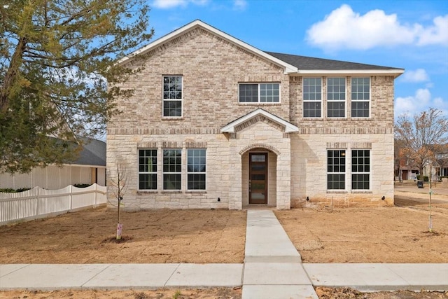 traditional-style house featuring stone siding, a shingled roof, fence, and brick siding