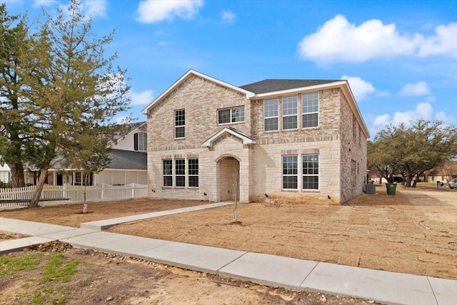 traditional home with stone siding, central AC unit, fence, and brick siding