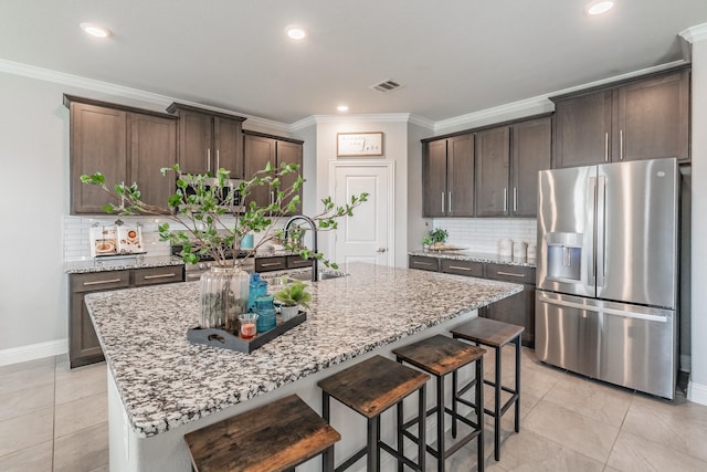 kitchen featuring stainless steel fridge, a center island with sink, light stone counters, and tasteful backsplash