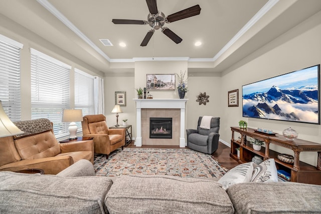 living room with light wood-type flooring, ornamental molding, a tray ceiling, ceiling fan, and a tiled fireplace