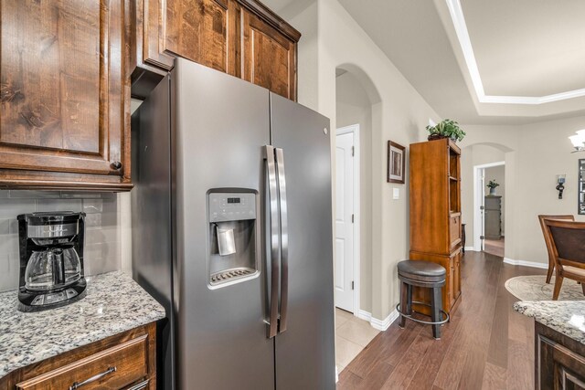 kitchen with stainless steel fridge, light stone countertops, light wood-type flooring, and tasteful backsplash