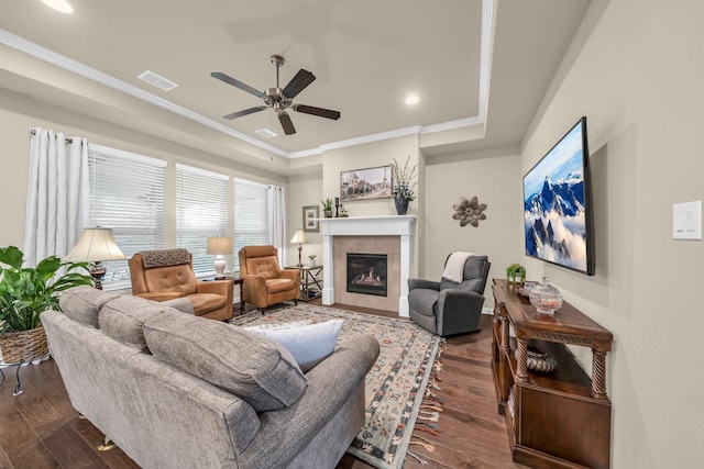 living room featuring dark hardwood / wood-style floors, ceiling fan, crown molding, and a tile fireplace