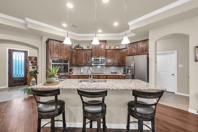 kitchen featuring appliances with stainless steel finishes, light stone counters, dark brown cabinetry, dark wood-type flooring, and an island with sink