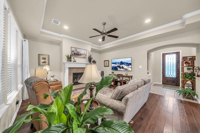 living room with a raised ceiling, crown molding, hardwood / wood-style flooring, ceiling fan, and a fireplace