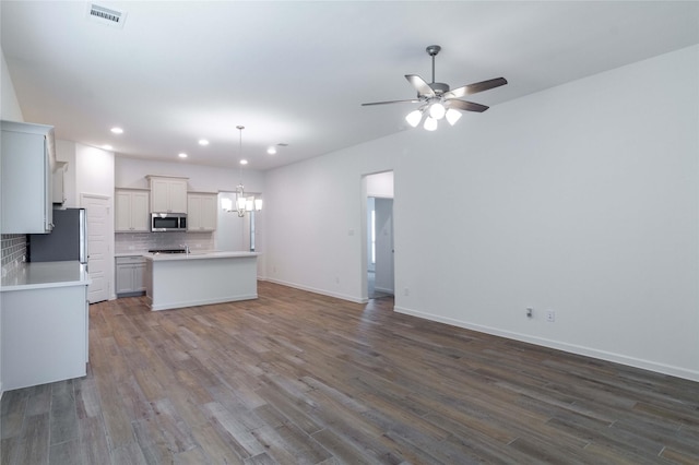 kitchen with white cabinets, decorative backsplash, appliances with stainless steel finishes, decorative light fixtures, and dark hardwood / wood-style flooring