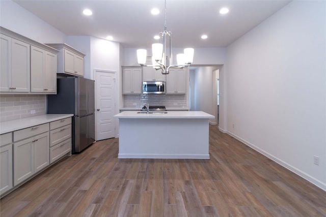 kitchen featuring gray cabinetry, hanging light fixtures, stainless steel appliances, dark hardwood / wood-style flooring, and a center island with sink