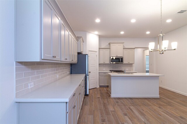 kitchen with stainless steel appliances, tasteful backsplash, an island with sink, pendant lighting, and light hardwood / wood-style floors