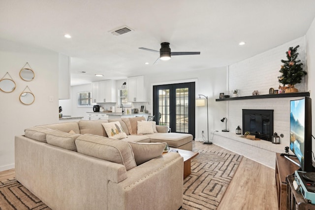 living room featuring sink, light hardwood / wood-style flooring, ceiling fan, a brick fireplace, and french doors