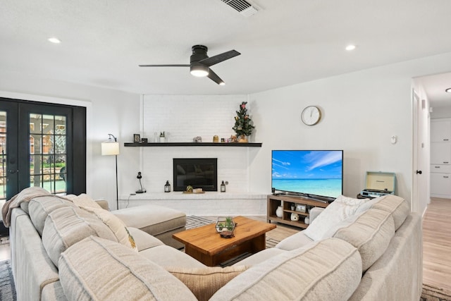 living room featuring a fireplace, light hardwood / wood-style floors, french doors, and ceiling fan