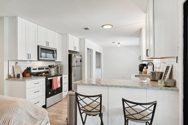 kitchen with appliances with stainless steel finishes, a breakfast bar area, white cabinets, and kitchen peninsula