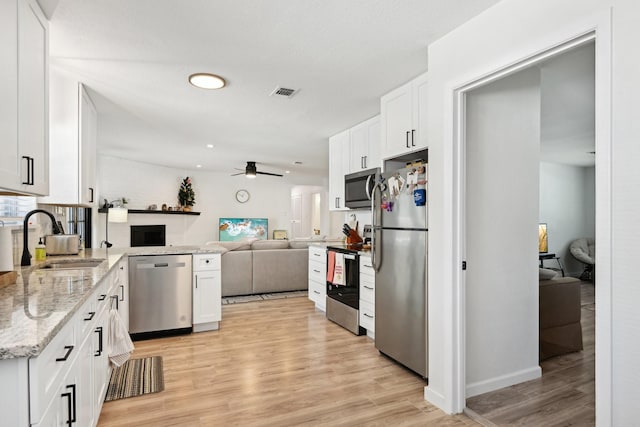 kitchen with sink, white cabinetry, light stone counters, light wood-type flooring, and stainless steel appliances