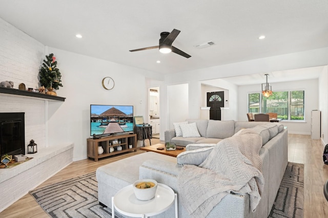 living room with ceiling fan, light hardwood / wood-style floors, and a brick fireplace