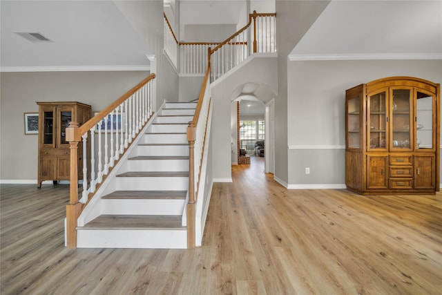 staircase with arched walkways, crown molding, baseboards, and wood finished floors