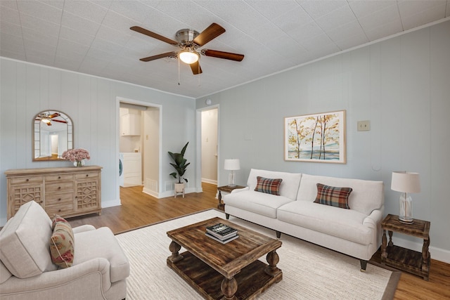 living room featuring ceiling fan, crown molding, wood walls, light hardwood / wood-style floors, and washer / dryer