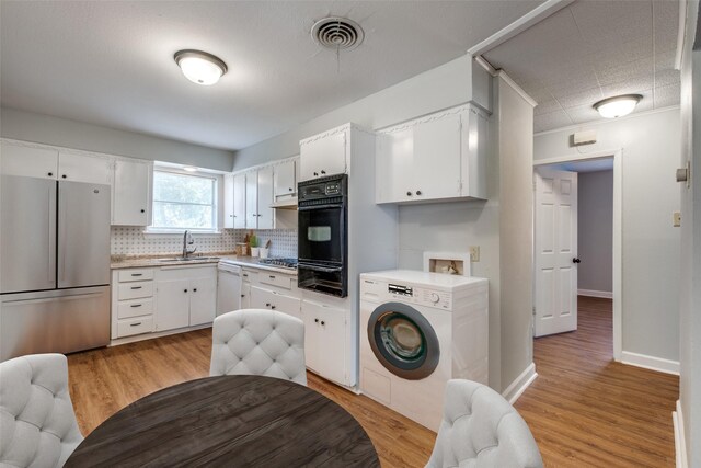 kitchen with light hardwood / wood-style floors, stainless steel appliances, sink, white cabinets, and washer / clothes dryer