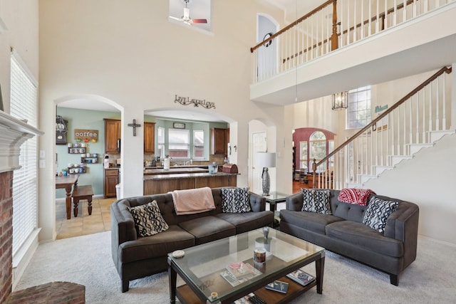 living room with ceiling fan with notable chandelier, light carpet, and a high ceiling