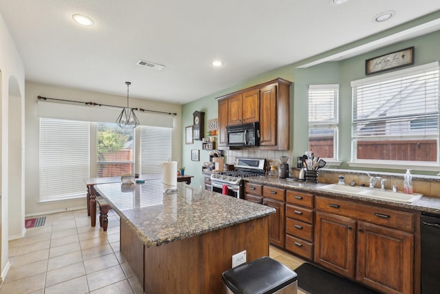 kitchen with black appliances, decorative light fixtures, a kitchen island, and a wealth of natural light