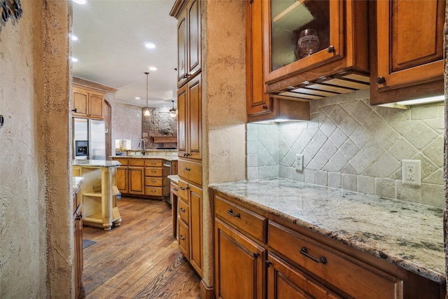 kitchen featuring stainless steel appliances, wood-type flooring, hanging light fixtures, and light stone counters