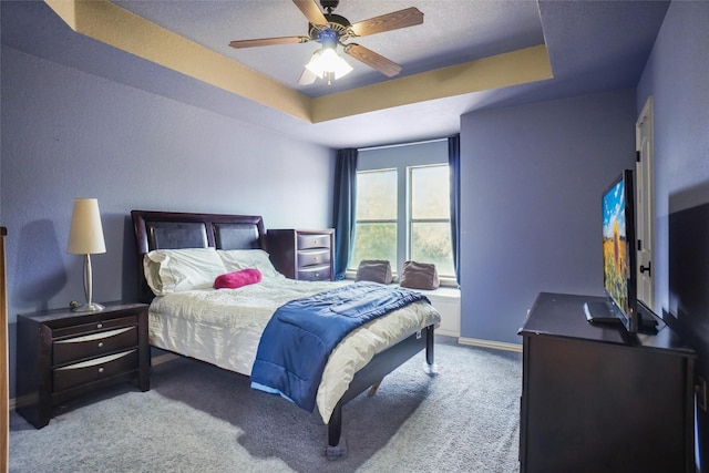 carpeted bedroom with a raised ceiling and ceiling fan