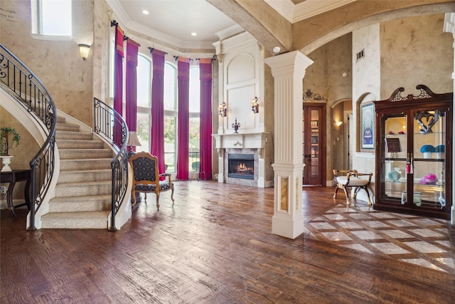 entrance foyer with hardwood / wood-style flooring, crown molding, a high ceiling, and ornate columns