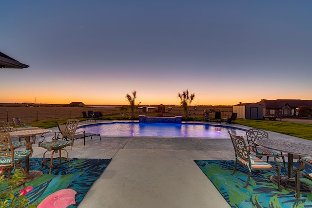 pool at dusk with pool water feature, a storage shed, and a patio