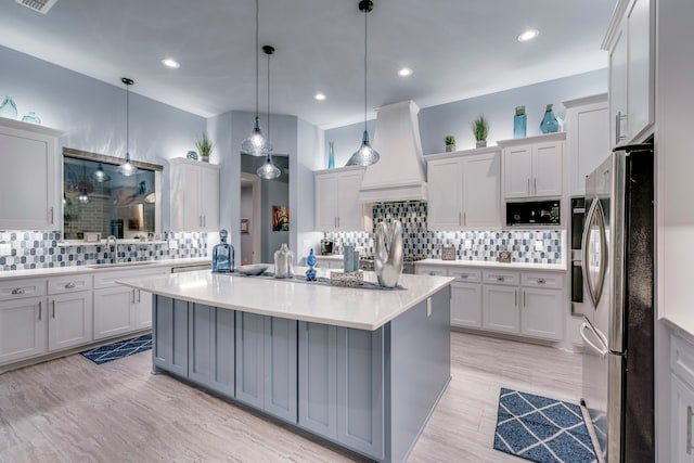 kitchen featuring a kitchen island, a sink, light countertops, freestanding refrigerator, and custom range hood