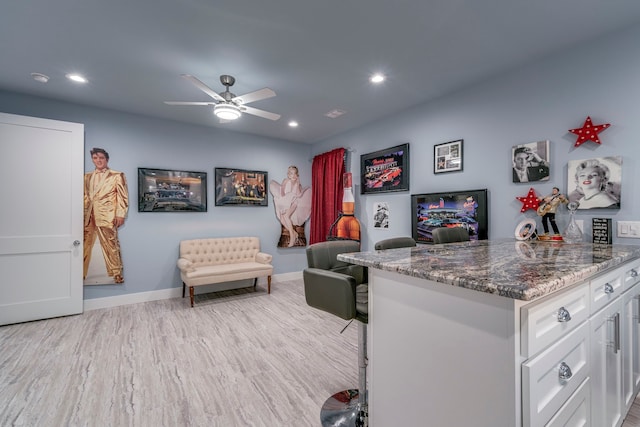 interior space with light hardwood / wood-style floors, ceiling fan, white cabinetry, and dark stone counters