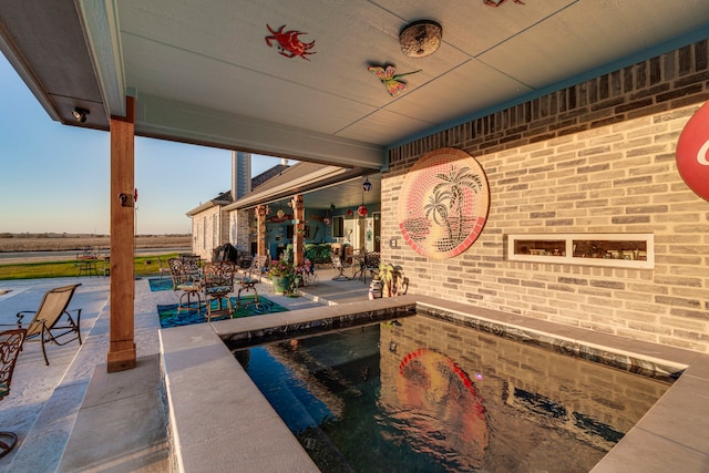 pool at dusk with a hot tub, a rural view, and a patio