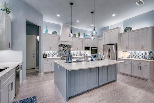 kitchen with decorative light fixtures, appliances with stainless steel finishes, custom range hood, and a kitchen island