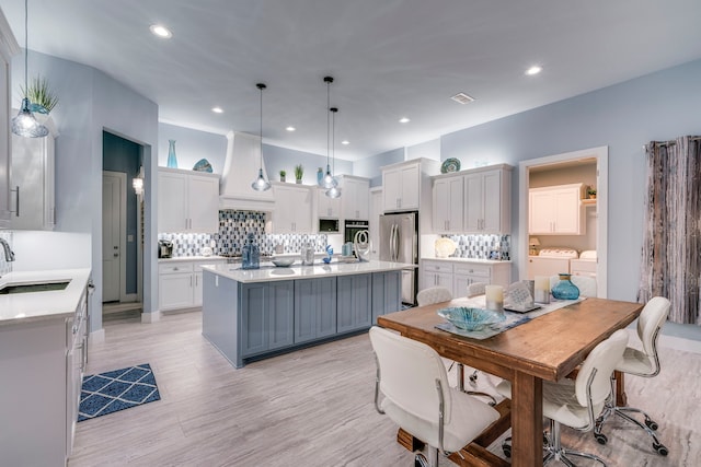 kitchen featuring separate washer and dryer, stainless steel appliances, an island with sink, sink, and hanging light fixtures