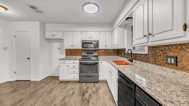 kitchen featuring light stone countertops, white cabinetry, sink, appliances with stainless steel finishes, and light wood-type flooring