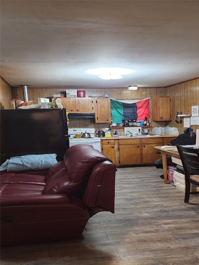 kitchen featuring white electric range, sink, wood walls, black refrigerator, and light hardwood / wood-style floors