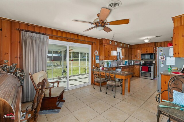 kitchen with wooden walls, stainless steel appliances, ceiling fan, and light tile patterned flooring