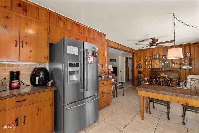 kitchen with stainless steel fridge with ice dispenser, light tile patterned floors, wooden walls, ceiling fan, and backsplash