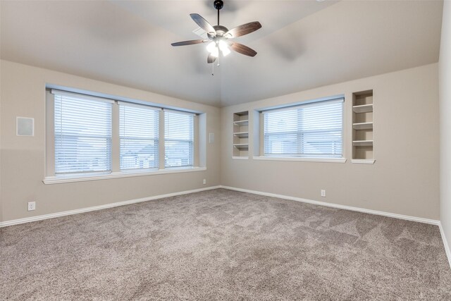 carpeted empty room featuring built in shelves, ceiling fan, and lofted ceiling