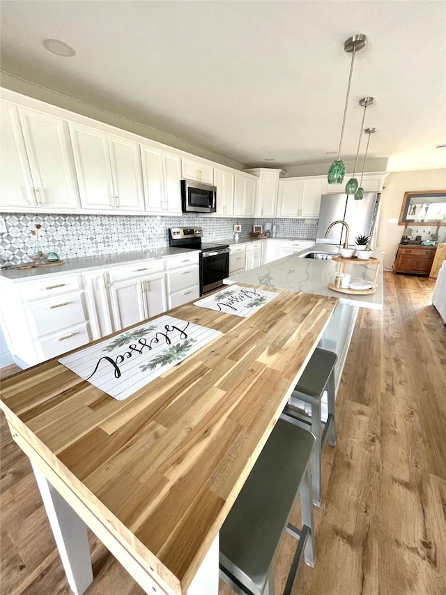 kitchen featuring white cabinetry, pendant lighting, stainless steel appliances, a kitchen island with sink, and decorative backsplash