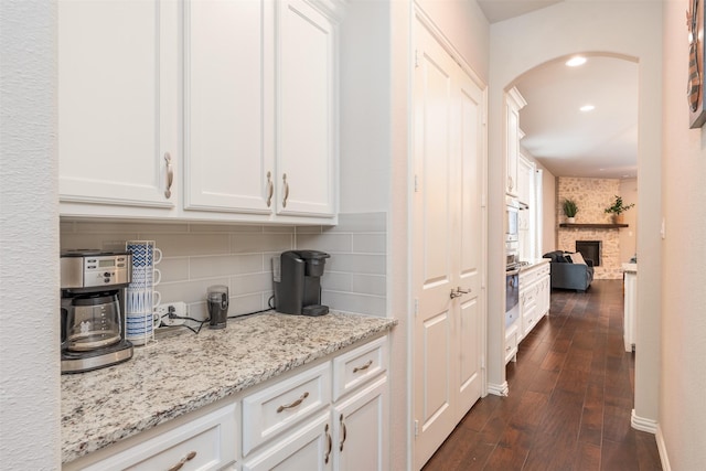 bar featuring light stone countertops, white cabinetry, a fireplace, and dark wood-type flooring