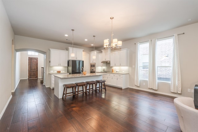 kitchen with white cabinets, decorative light fixtures, stainless steel appliances, and an island with sink