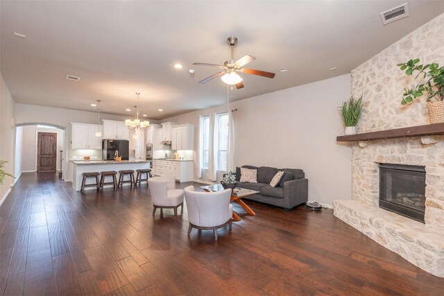 living room with ceiling fan with notable chandelier, dark hardwood / wood-style flooring, and a fireplace