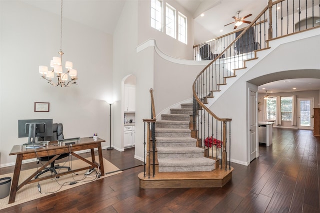 stairway with ceiling fan with notable chandelier, wood-type flooring, and high vaulted ceiling