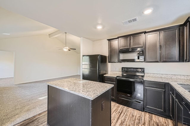 kitchen with light stone countertops, black appliances, lofted ceiling with beams, light hardwood / wood-style floors, and a kitchen island