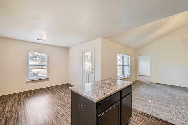 kitchen featuring light stone countertops, dark brown cabinets, vaulted ceiling, dark wood-type flooring, and a kitchen island