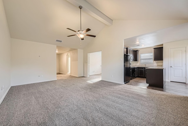 unfurnished living room with carpet, ceiling fan, beamed ceiling, and sink