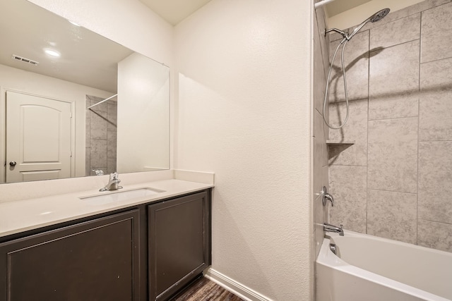 bathroom with wood-type flooring, vanity, and tiled shower / bath