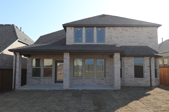 rear view of house featuring a shingled roof, a patio area, and brick siding