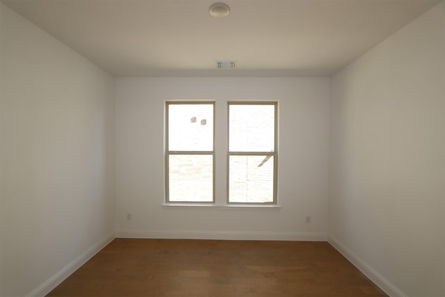 empty room with baseboards, wood finished floors, visible vents, and a healthy amount of sunlight