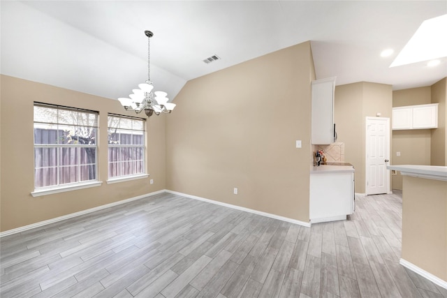 unfurnished room featuring lofted ceiling with skylight, light hardwood / wood-style flooring, and an inviting chandelier