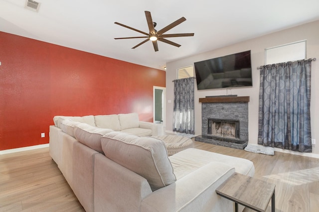 living room featuring light hardwood / wood-style flooring, ceiling fan, and a stone fireplace