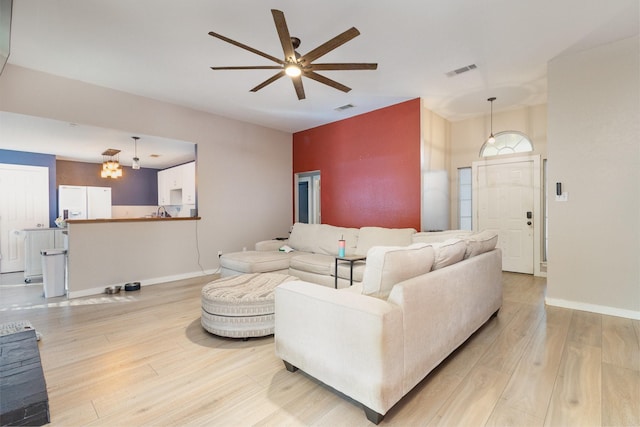 living room featuring ceiling fan with notable chandelier and light wood-type flooring